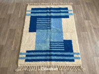 Handwoven Custom Beni Ourain Moroccan Rug showing plush cream wool pile and geometric diamond pattern in Moroccan blue, Malibu blue, and Sky blue yarn with traditional fringe.