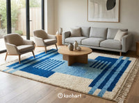 Large custom Moroccan area rug anchors a modern bohemian living room, featuring a cream base with blue diamond motifs under a white linen sofa and reclaimed wood coffee table.