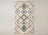 Custom made Beni Ourain Moroccan wool rug flat lay featuring organic flowing lines in dusty blue grey and cool grey against a natural cream shaggy base with traditional fringe.