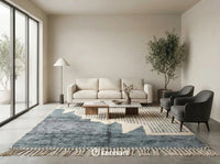 Large custom Beni Ourain area rug with charcoal and blue-grey diamonds anchoring a minimalist living room with a cream linen sofa and wooden coffee table.