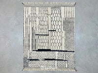 Custom made Beni Ourain Moroccan rug flat lay showing plush cream wool texture and charcoal geometric diamond pattern with traditional fringe detail.